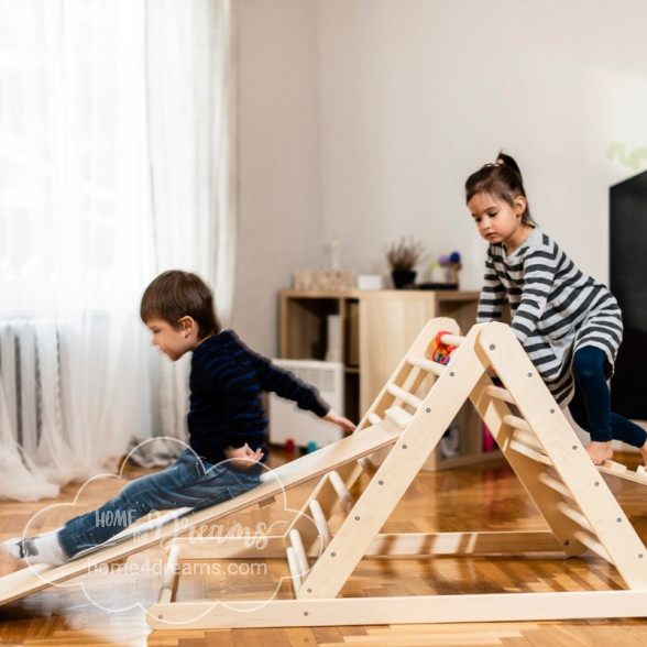 Children playing on a Pikler triangle climbing toy with a slide board